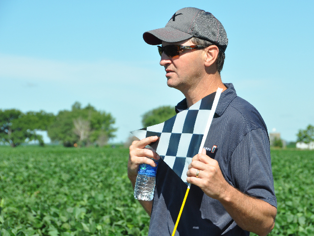 Monsanto representative Chris Mayo displays the black-and-white checkered flag that will mark the company&#039;s dicamba-tolerant crops in the future. (DTN photo by Emily Unglesbee)